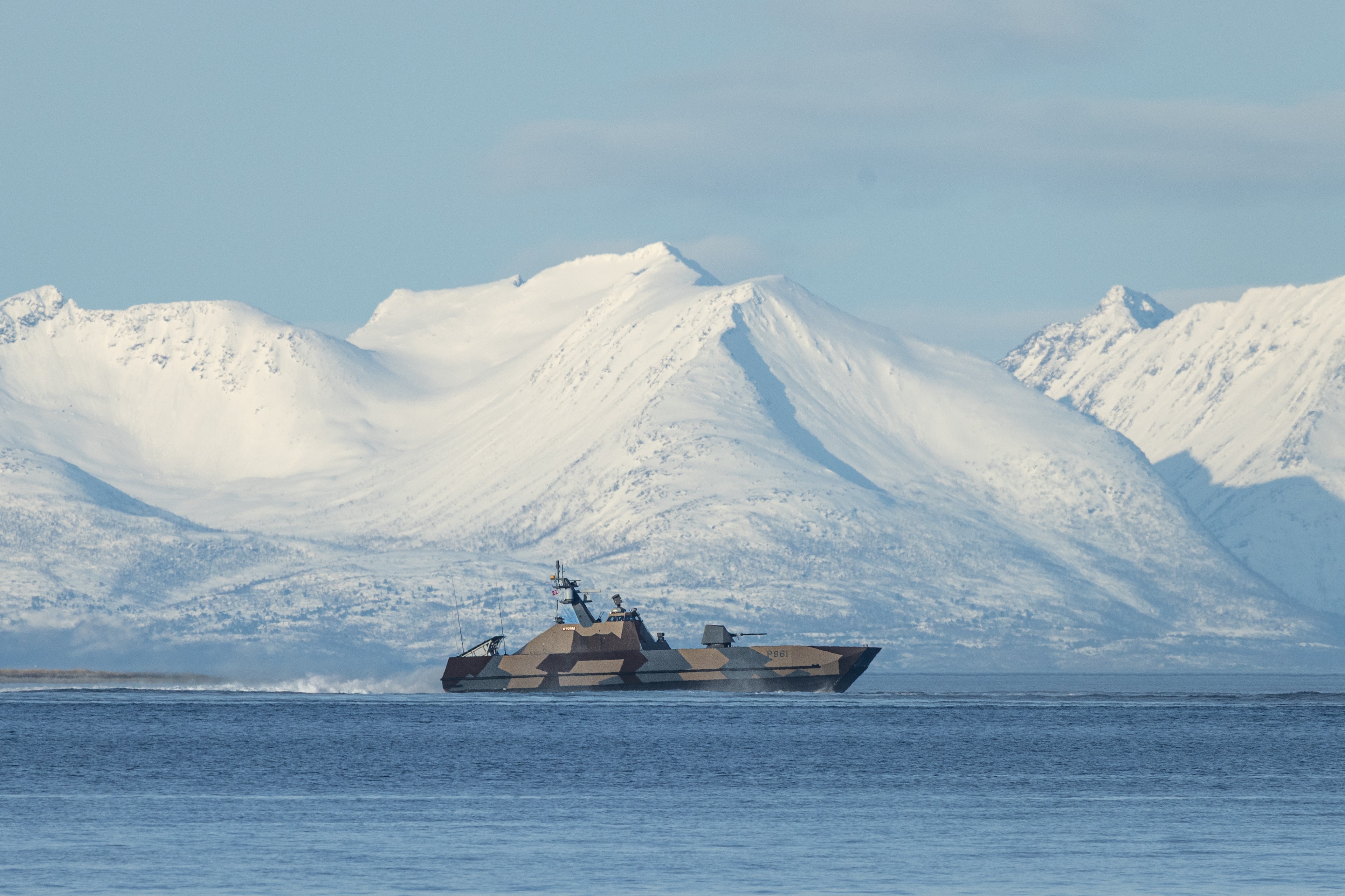 Fartøy på kaldt hav foran snødekte fjell.